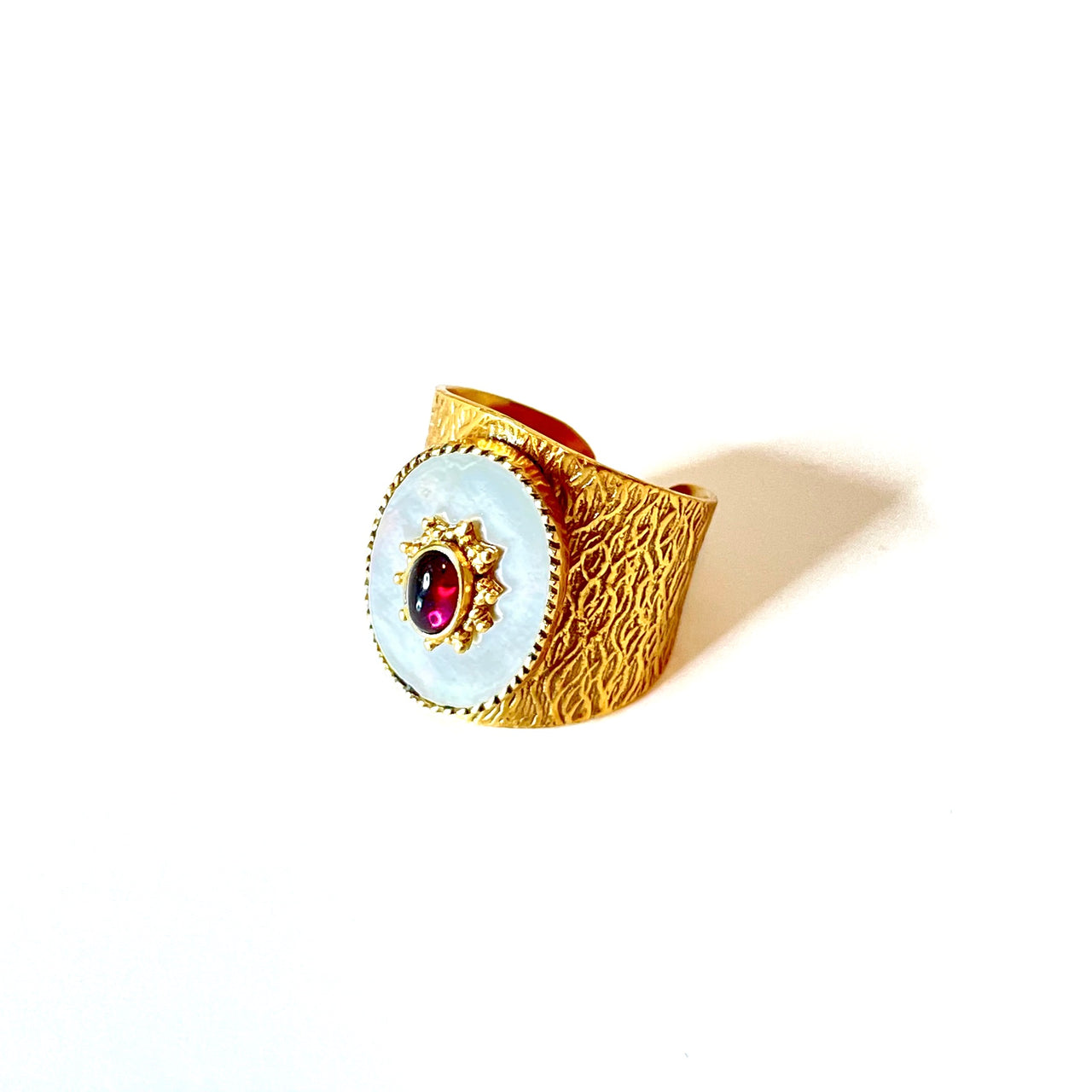 Espectacular anillo de bronce con baño de oro. El detalle central es de nacar con un rubí. Este anillo es ajustable lo que lo hace perfecto. Además es super combinable con tu look favorito. Lateral